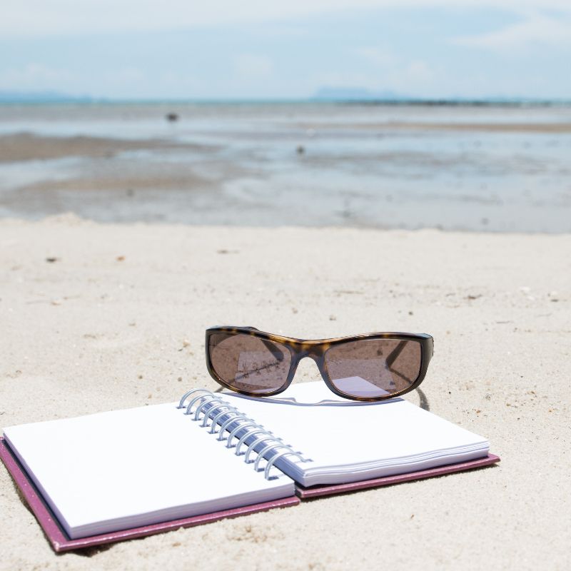 Cuaderno y gafas en la orilla d ela playa